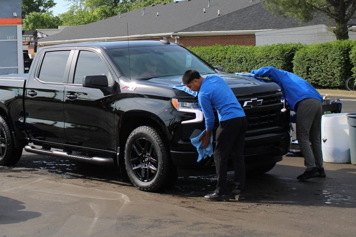 Two Lexington Auto Spa staff hand-drying the hood of a black Chevrolet Silverado with microfiber towels