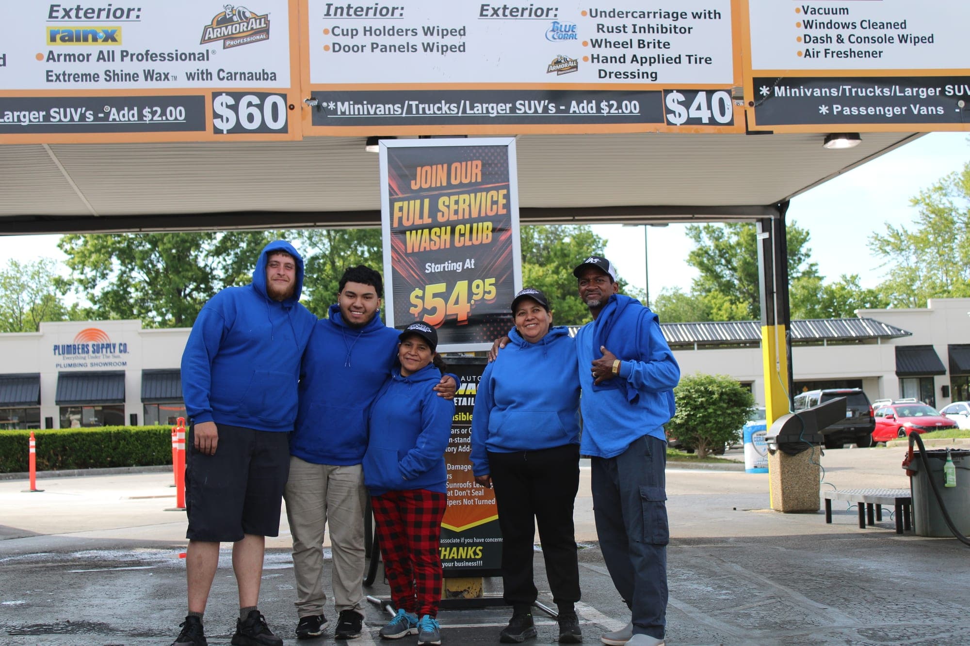 Five Lexington Auto Spa staff in blue hoodies standing under the wash price signs